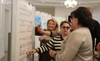 Three women stand inside looking at a poster and having a discussion about its content.